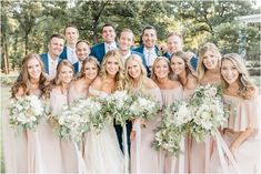 a group of people standing next to each other in front of trees and bushes with bouquets