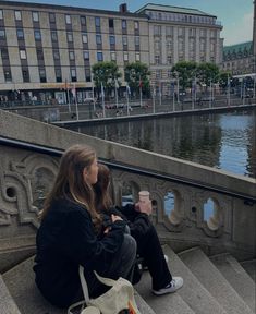 a woman sitting on steps next to a body of water with buildings in the background