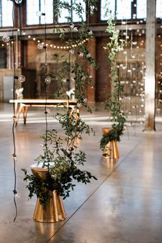 some plants are in gold vases on the floor with string lights hanging from them