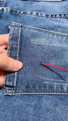 someone is stitching the red thread into their jeans pocket with one thumb and two fingers