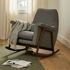 a rocking chair with a blanket on top of it next to a book and window