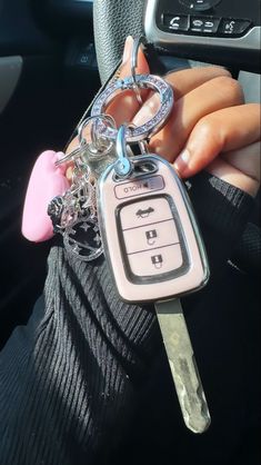 a person holding a car key chain in their hand and wearing a pink heart charm