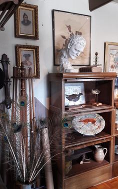 an antique china cabinet with peacock feathers on the bottom shelf and other items in front of it