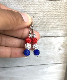 a person is holding two red, white and blue beaded earrings in their hand