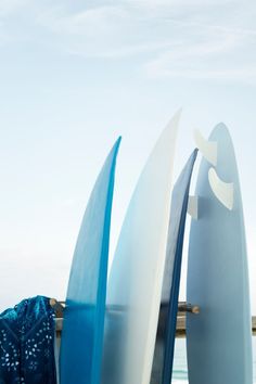 three surfboards leaning against each other in front of the ocean on a sunny day