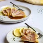 two white plates topped with slices of meat and lemon wedges next to each other