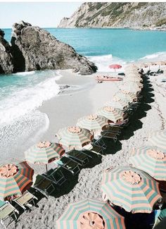 beach chairs and umbrellas are lined up on the sand near the water's edge