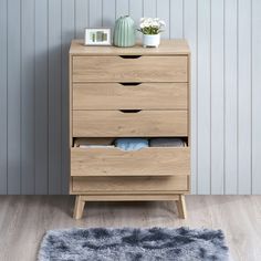 a wooden chest of drawers in a room with a rug and vase on the floor