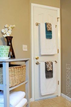 two towels are hanging on the door and in front of a basket with white flowers