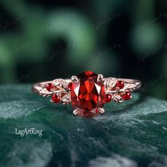 a close up of a ring with a red stone in the middle and leaves around it