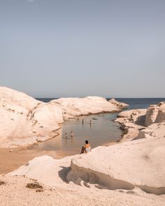 some people are playing in the water near white cliffs and blue skies on a sunny day