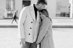 a man and woman standing next to each other in front of a building with people walking by