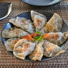 a plate of dumplings with carrots and seasoning sitting on a place mat