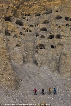 some people are walking on the side of a hill with holes in it and there is a mountain behind them