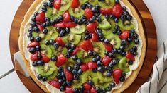 a pizza topped with kiwis and blueberries on top of a wooden cutting board