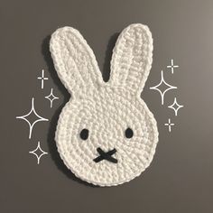 a white crocheted bunny face on a gray surface with stars in the background