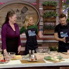 three people standing in front of a table with food on it and one person wearing an apron