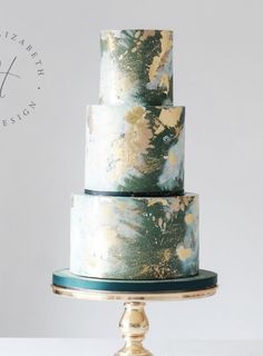 a three - tiered cake with gold and green designs on the top is sitting on a stand