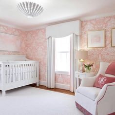 a baby's room with pink and white wallpaper, a crib, and a chandelier