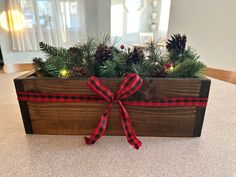 a wooden planter with pine cones and evergreens tied around the top, sitting on a table