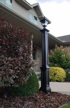 a black lamp post in front of a house with bushes and shrubs around the corner