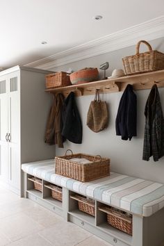 a bench with baskets and coats hanging on the wall next to it in a room