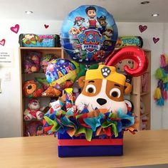 a dog in a box with balloons and other items on the shelf behind it at a children's birthday party