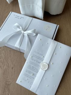 an open white wedding card with pearls and a ribbon on the inside is sitting on a table