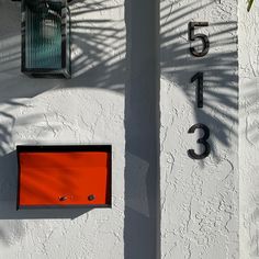 an orange box is on the side of a white building with two black numbers and a palm tree