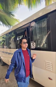 a man standing next to a white bus with sunglasses on it's face and palm trees in the background