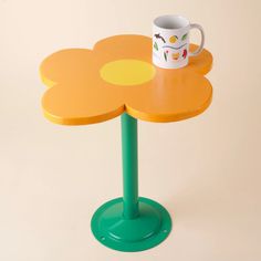 a yellow flower shaped table with a coffee cup on it's top and a green base