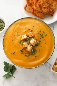 a bowl of carrot soup with toasted bread on the side and green garnish