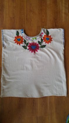 "Gorgeous ivory cotton wide style embroidered hippie blouse. Heavily decorated with flowers and hearts in colourful embroidery around the front and back of neck. Sleeves have simple blue stitching as does the round neck. arm hole to arm hole 23\" (up to bust 46) length 25\", blouse is same width all the way down. ** A very faint 'run' of the pink flower dye, but barely visible as shown in photos**" Bohemian Tops With Geometric Embroidery And Crew Neck, Bohemian Crew Neck Top With Geometric Embroidery, Bohemian Long Sleeve Tops With Machine Embroidery, Bohemian Crew Neck Blouse With Floral Embroidery, White Hippie Peasant Top For Festival, Bohemian Tops With Multicolor Embroidery And Embroidered Hem, Bohemian Cotton Tops With Machine Embroidery, Bohemian Tops With Machine Embroidery, Bohemian Tops With Multicolor Embroidery