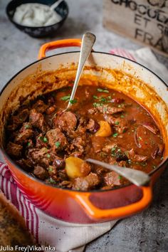 a large pot filled with stew on top of a table next to a wooden spoon