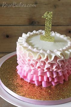 a pink and gold cake with a number one on top is sitting on a plate