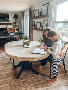 a woman and child sitting at a table in the middle of a room with pictures on the wall