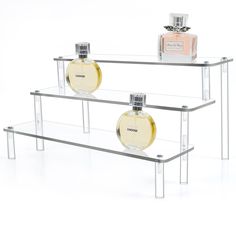 two clear shelves with perfume bottles on top of each shelf in front of white background