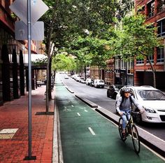 a man riding a bike down a street next to tall buildings and parked cars on the side of the road