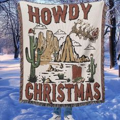 a person standing in the snow holding up a christmas banner with cactus and mountains on it