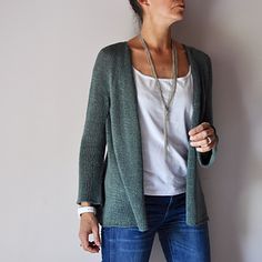 a woman standing in front of a wall wearing a green cardigan sweater and jeans