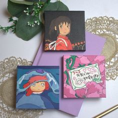 three cards with anime characters on them are sitting next to some flowers and a lace doily