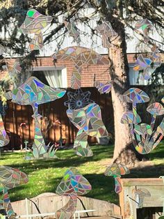 a group of stained glass pieces hanging from a tree branch in front of a house