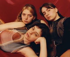 three young women are posing for the camera in front of a red background and one is leaning on her head