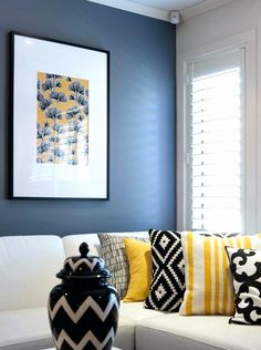 a living room with blue walls and white couches, black and yellow throw pillows