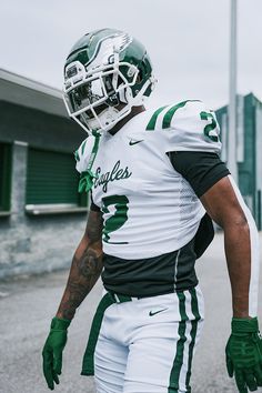 a football player wearing a green and white uniform is walking down the street with his hand on his hip