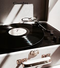 a record player sitting on top of a white suitcase next to a pair of glasses