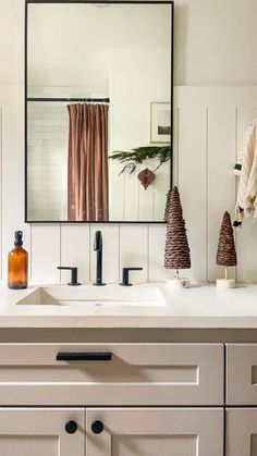 a bathroom sink with a mirror above it and two trees on the counter next to it