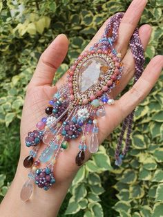 a hand holding a beaded bracelet in front of some bushes