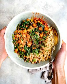 two hands holding a bowl of food with spinach and chickpeas in it