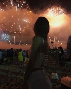 a woman standing on top of a sandy beach next to a crowd of people watching fireworks